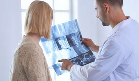 Handsome doctor is talking with young female patient and making notes while sitting in his office.の写真素材