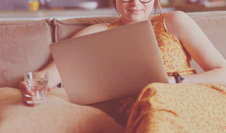 Beautiful young woman sitting on a sofa and working on a laptopの写真素材