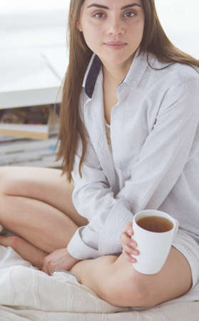 Woman sitting in bed reading a book and having breakfastの写真素材