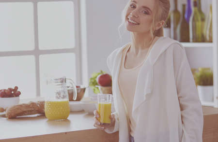 Attractive woman holding a glass of orange juice while standing in the kitchenの写真素材