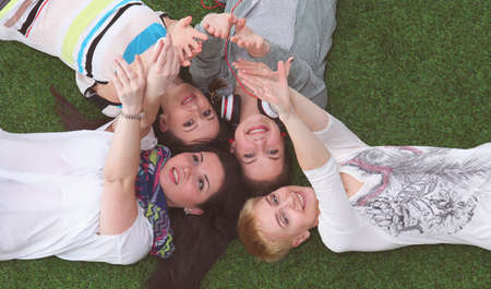 Four young women lying on green grass with hands upの写真素材