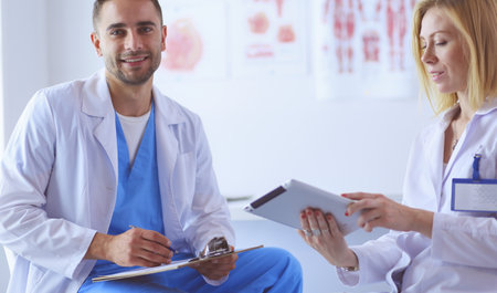 Handsome doctor is talking with young female patient and making notes while sitting in his officeの写真素材