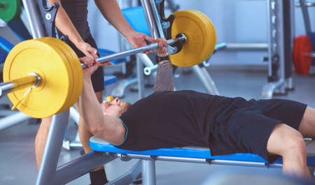 Young man lifting the barbell in gym with instructorの写真素材