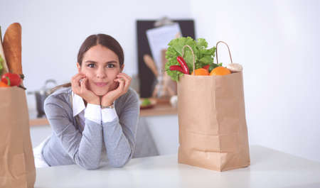 Young woman holding grocery shopping bag with vegetables . Standing in the kitchenの写真素材