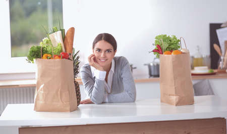Young woman holding grocery shopping bag with vegetables . Standing in the kitchenの写真素材