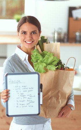 Young woman holding grocery shopping bag with vegetables . Standing in the kitchenの写真素材