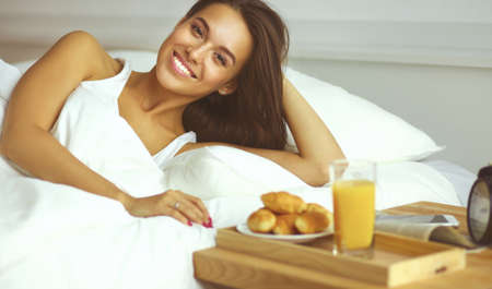 Beautiful young woman sitting in bed and having breakfastの写真素材