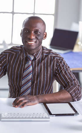 Handsome afro american businessman in classic suit is using a laptop and smiling while working in officeの写真素材