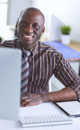 Handsome afro american businessman in classic suit is using a laptop and smiling while working in officeの写真素材