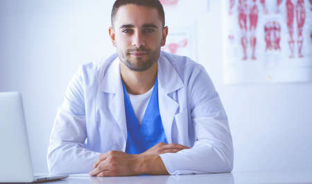 Portrait of a male doctor with laptop sitting at desk in medical officeの写真素材