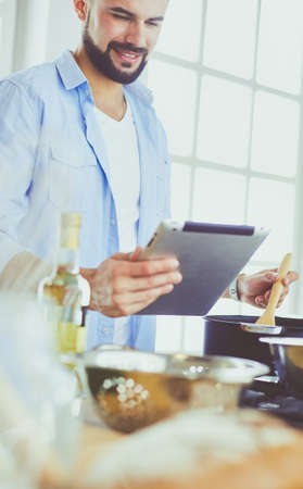 Man following recipe on digital tablet and cooking tasty and healthy food in kitchen at homeの写真素材