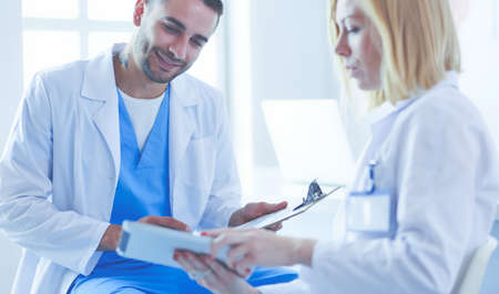 Handsome doctor is talking with young female doctor and making notes while sitting in his office.の写真素材