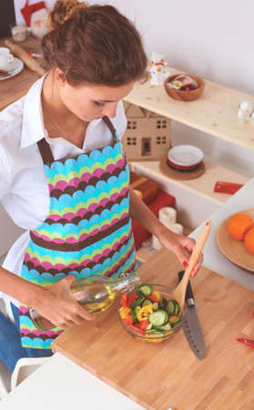 Young woman mixing fresh salad standing near deskの写真素材