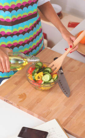 Young woman mixing fresh salad standing near deskの写真素材