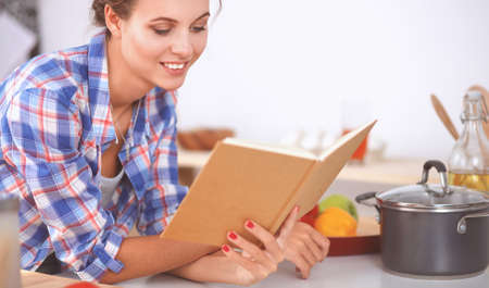 Young woman reading cookbook in the kitchen, looking for recipeの写真素材