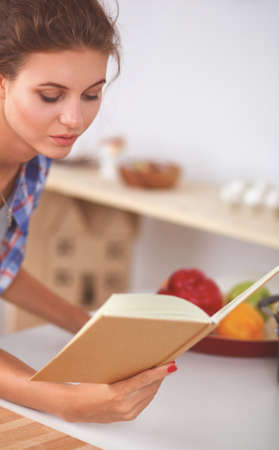 Young woman reading cookbook in the kitchen, looking for recipeの写真素材