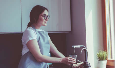 Woman filling a glass of water from a stainless steel or chrome tap or faucetの写真素材