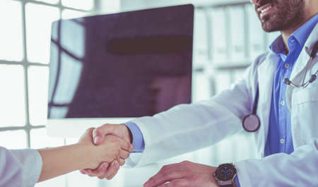 Doctor shaking hands to patient in the office at deskの写真素材
