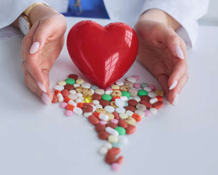Cardiologist with red heart and stethoscope at tableの写真素材