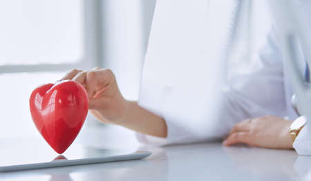 Female doctor with stethoscope holding heart, on light backgroundの写真素材