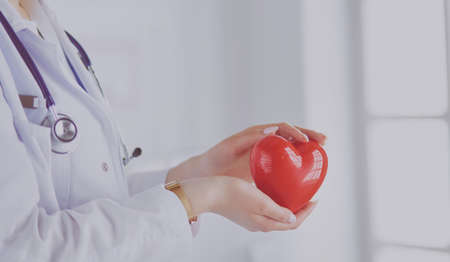Female doctor with stethoscope holding heart, on light backgroundの写真素材