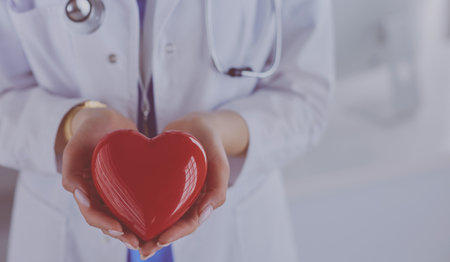 Female doctor with stethoscope holding heart, on light backgroundの写真素材