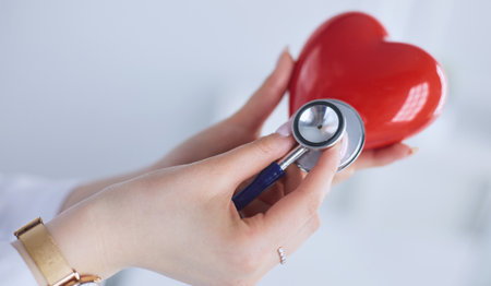 A doctor with stethoscope examining red heart, isolated on white backgroundの写真素材