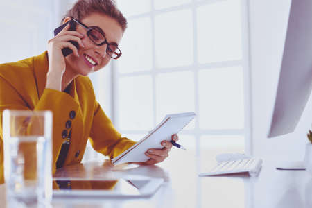 Portrait of beautiful woman making call while sitting at her workplace in front of laptop and working on new projectの写真素材