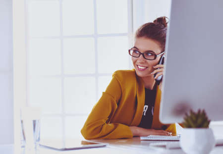 Businesswoman sitting in office with laptop on telephoneの写真素材
