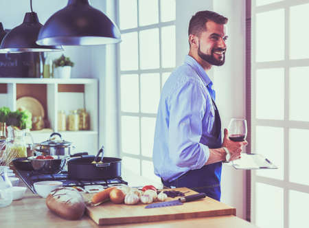 Man following recipe on digital tablet and cooking tasty and healthy food in kitchen at homeの写真素材