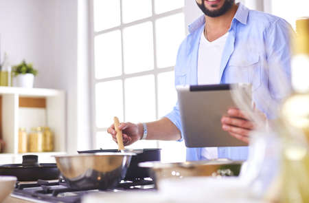 Man following recipe on digital tablet and cooking tasty and healthy food in kitchen at homeの写真素材