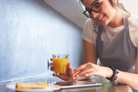 Portrait of young attractive caucasian brunette housewife at kitchen. Morning with cup of coffee and tablet pcの写真素材