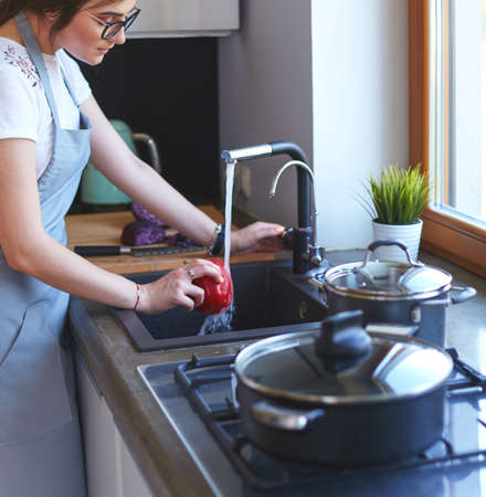 Woman washing vegetables. Beautiful young woman washing vegetables for salad and smiling while standing in the kitchenの写真素材