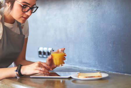 Attractive woman holding a glass of orange juice while standing in the kitchenの写真素材