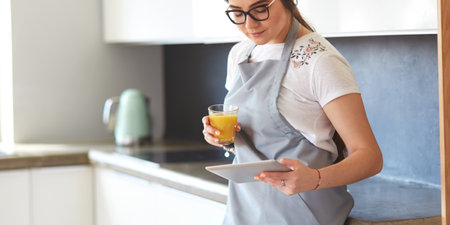 Young woman with orange juice and tablet in kitchenの写真素材