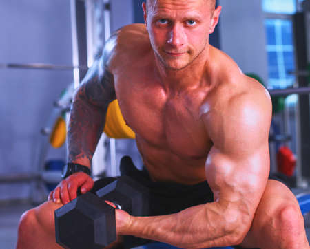 Strong man, bodybuilder exercising with dumbbells in a gymの写真素材