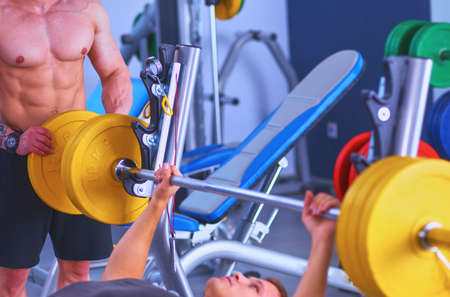 Young man lifting the barbell in gym with instructorの写真素材