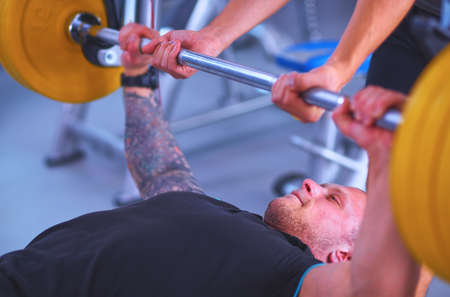 Young man lifting the barbell in gym with instructorの写真素材