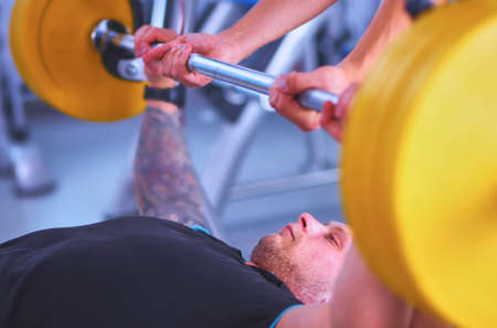 Young man lifting the barbell in gym with instructorの写真素材