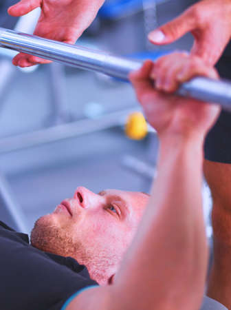 Young man lifting the barbell in gym with instructorの写真素材