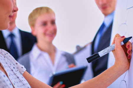 Businesswoman writing on flipchart while giving presentation to colleagues in officeの写真素材