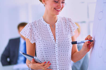 Businesswoman writing on flipchart while giving presentation to colleagues in officeの写真素材