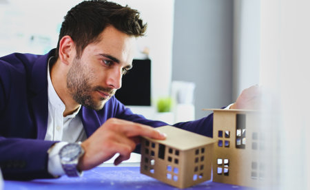 Businessman holding house miniature on hand standing in office.の写真素材