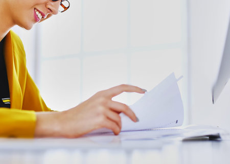 Beautiful young businesswoman doing some paperwork while sitting at office desk in front of laptop