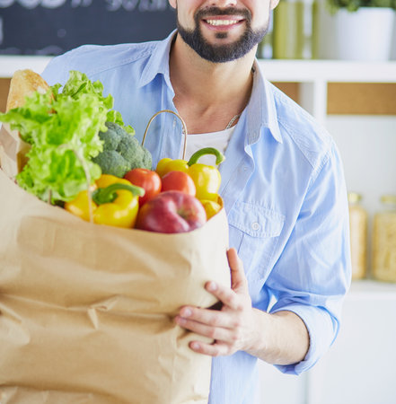 Man holding paper bag full of groceries on the kitchen background. Shopping and healthy food conceptの写真素材
