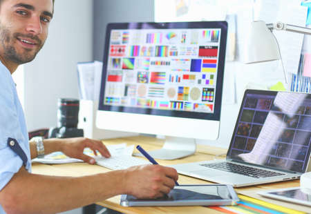 Portrait of young designer sitting at graphic studio in front of laptop and computer while working online.の写真素材