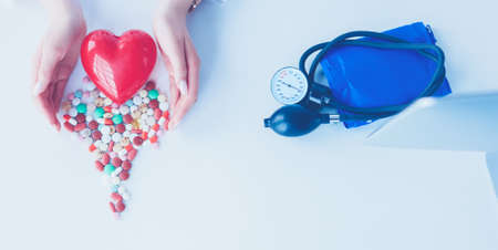 Cardiologist with red heart and stethoscope at tableの写真素材
