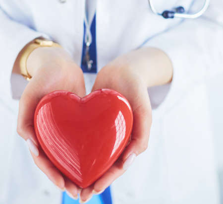 Female doctor with stethoscope holding heart, on light backgroundの写真素材