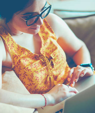 Young woman sitting on couch working on laptop computer at homeの写真素材