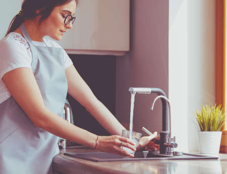 Human hand holding glass pouring fresh drink water at kitchen faucetの写真素材